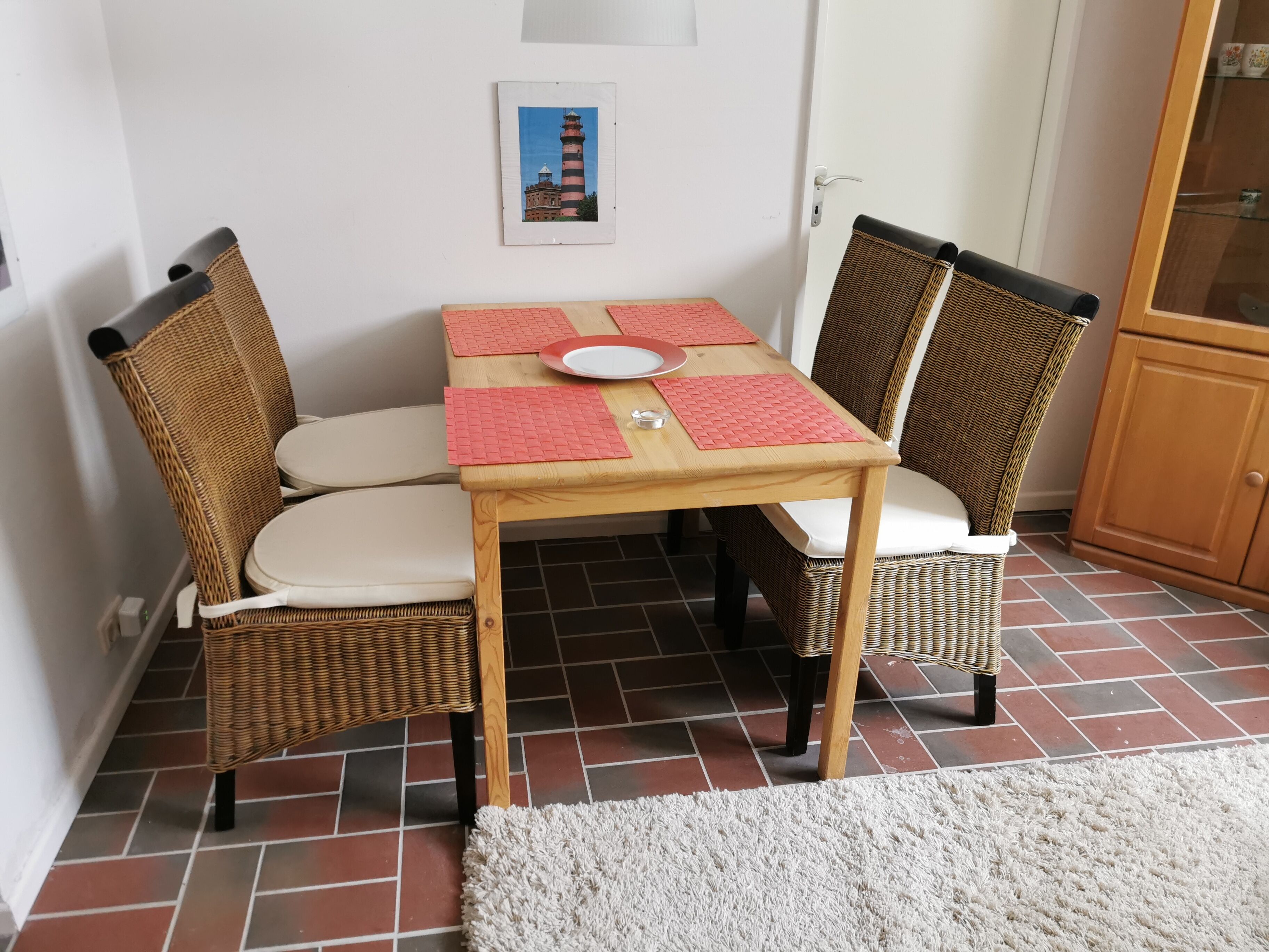 A dining area with a wooden table, four wicker chairs, and a white rug.
