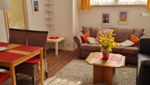 A living room with a wooden dining table, wicker chairs, a sofa, and a small coffee table with a vase of flowers.