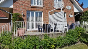 A two-story brick house with a white exterior, a balcony with a white railing, and a small garden area in front.