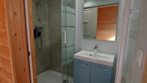 Casa de banho com cabine de chuveiro em vidro, lavatório e espelho.