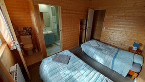 Quarto de cabana de madeira com duas camas, banheiro e uma pequena cozinha.