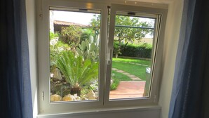 A sliding glass door with a view of a garden with various plants and a pathway. - Il Veliero Appartamento  con Giardino (Terracina)