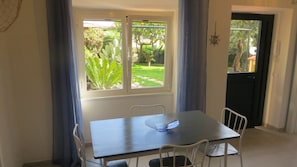 Zona de menjador amb taula i cadires, una finestra amb vista a un jardí i una porta que dóna a l'exterior.