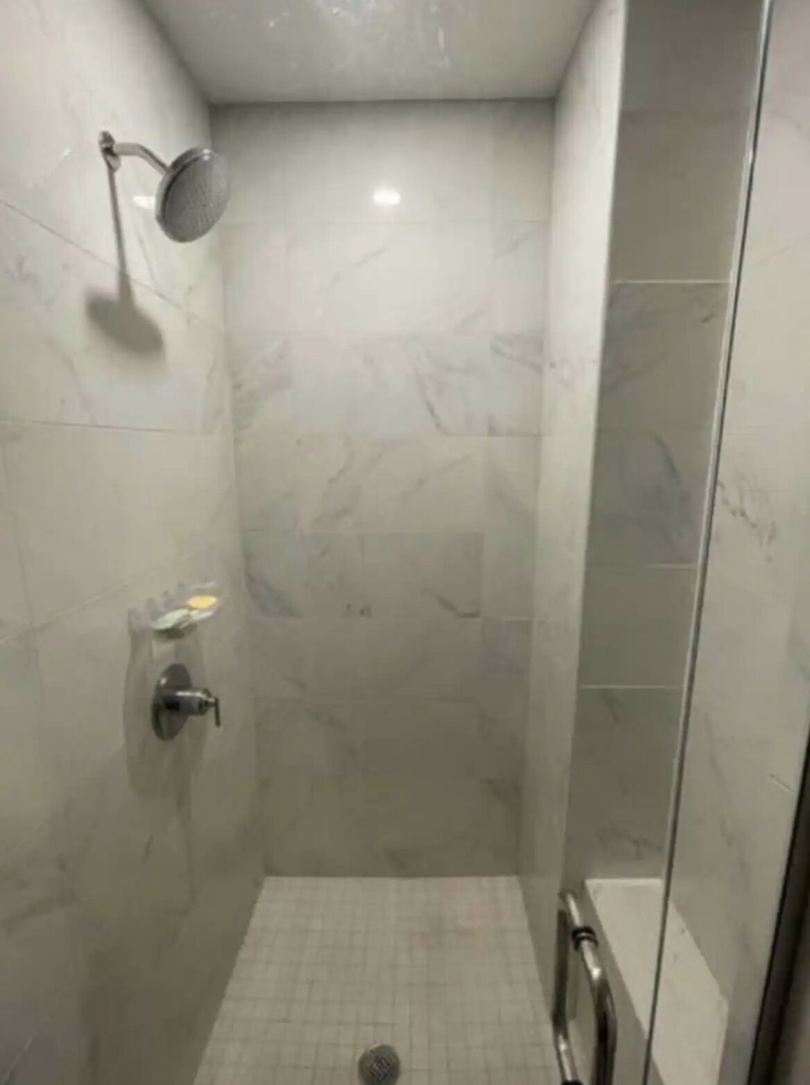 A small, tiled shower stall with a handheld showerhead, a soap dish, and a handheld shower control.