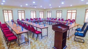Sala de conferências com várias mesas e cadeiras, um púlpito e amplas janelas com persianas.