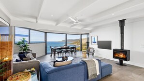 A modern living room with a large window overlooking the sea, a fireplace, and a dining area with a view.