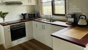 A compact kitchen with white cabinets, a built-in oven, a microwave, a kettle, and a window providing natural light. - Peaceful & Picturesque Farm Stay Only 5 Mins Drive From Benalla Township (Benalla)