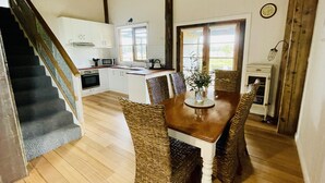 A kitchen with white cabinets, a wooden staircase, and a dining area with wicker chairs and a table. - Peaceful & Picturesque Farm Stay Only 5 Mins Drive From Benalla Township (Benalla)