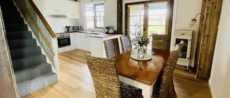 A kitchen with white cabinets, a wooden staircase, and a dining area with wicker chairs and a table.