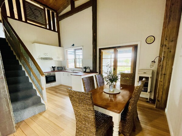 A kitchen with white cabinets, a wooden staircase, and a dining area with wicker chairs and a table.