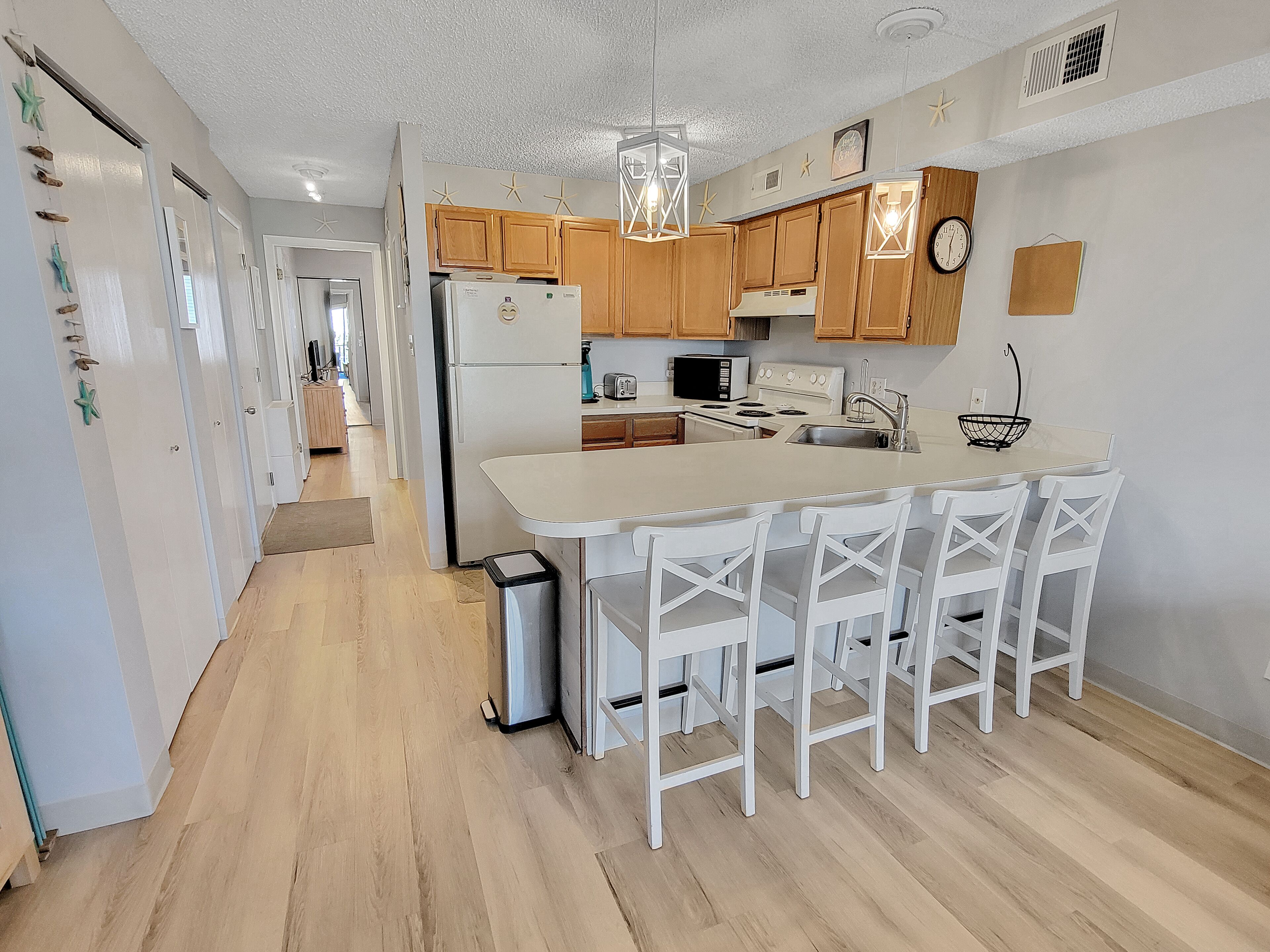 A modern kitchen with wooden cabinets, a central island with bar stools, a refrigerator, a stove, and a sink.