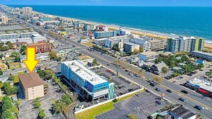 Vista aérea de uma cidade costeira com um edifício azul de destaque, marcado por uma seta amarela.