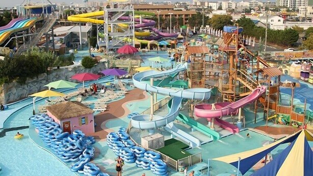 Um parque aquático com vários toboáguas e piscinas, rodeado por edifícios.