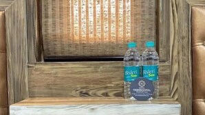 A wooden shelf with two Bisleri water bottles, a power outlet, and a small table with glasses and a tissue box. - Hotel YashoGopal Resortico (Mathura)