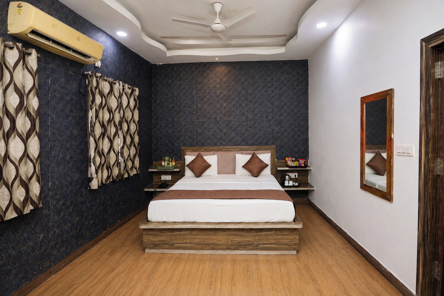 A bedroom with a bed, nightstands, a mirror, and an air conditioning unit.