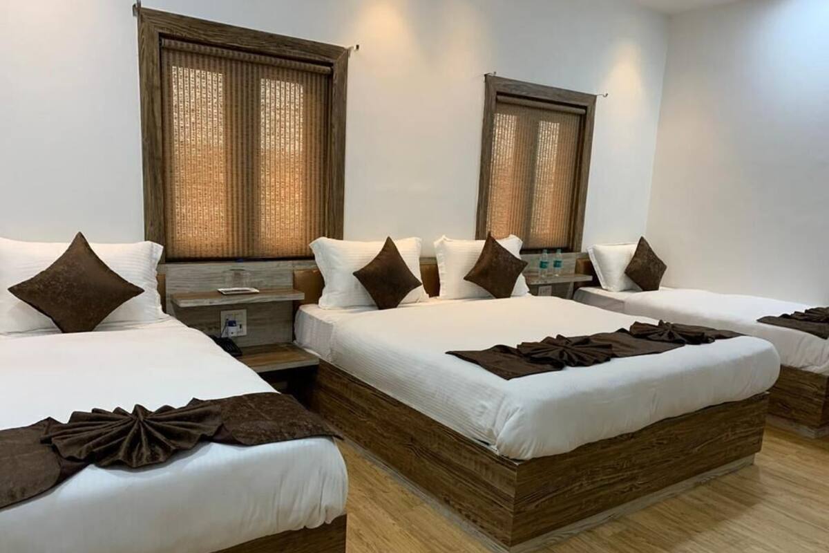 A hotel room with four beds arranged in a row, wooden headboards, and large windows with curtains.