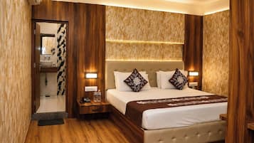 Habitación de hotel con cama, mesitas de noche, tocador, espejo y baño con lavamanos e inodoro.
