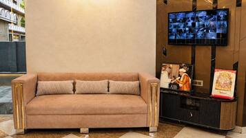 Un vestíbulo moderno con un sofá color crema, un televisor de pared y un objeto decorativo.
