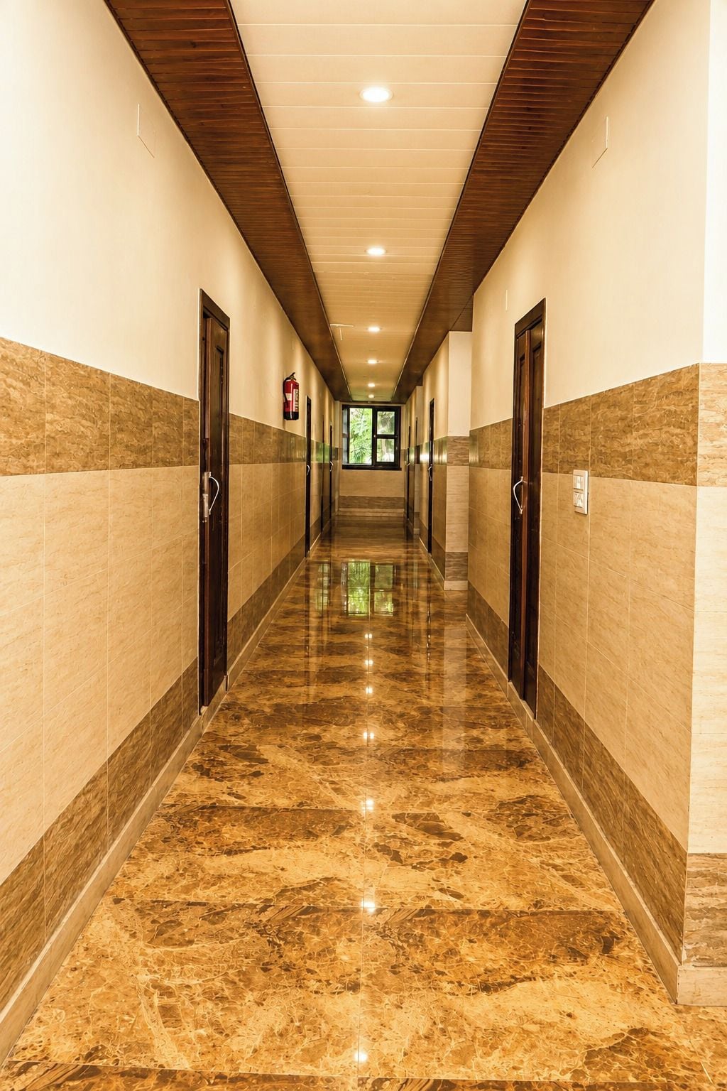A hotel corridor with a marble floor, wooden ceiling, and doors on both sides.