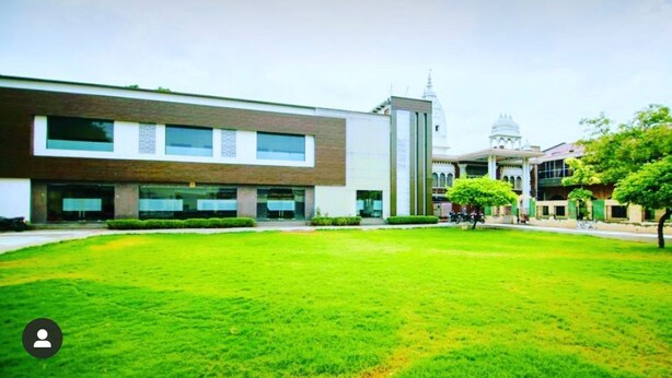 A modern building with a large grassy courtyard, a dome-shaped structure in the background, and a few trees. - Hotel YashoGopal Resortico (Mathura)