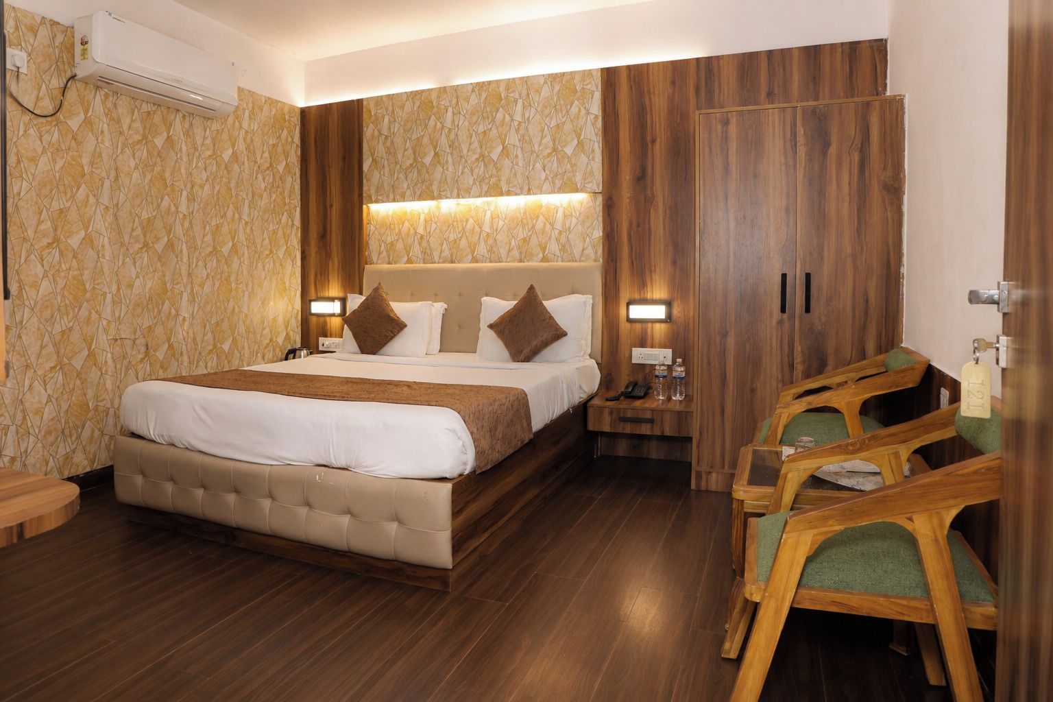 Una habitación de hotel con una cama grande, un armario de madera, mesitas de noche y un área de descanso con sillas.