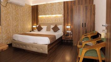Una habitación de hotel con una cama grande, un armario de madera, mesitas de noche y un área de descanso con sillas.