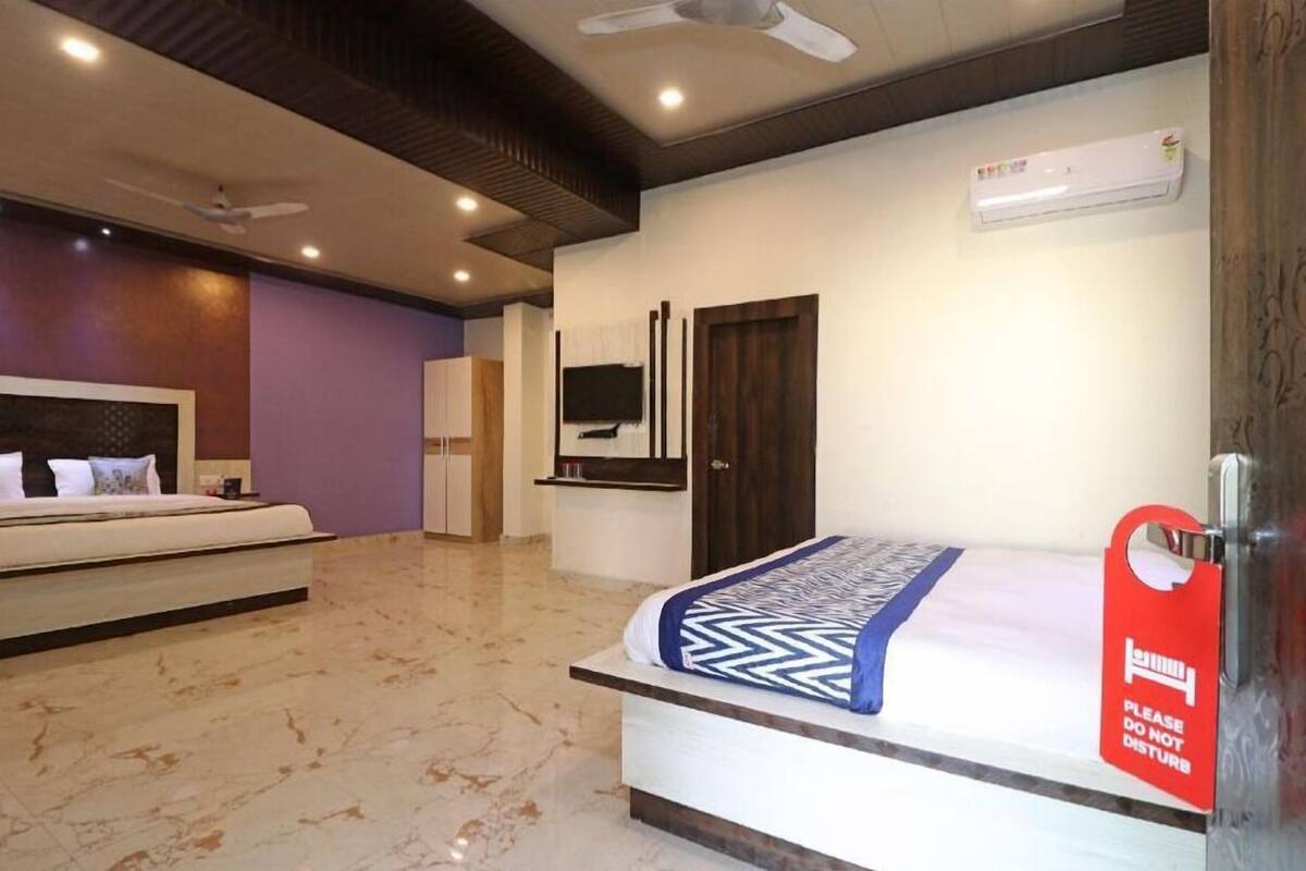A hotel room with a bed, a TV, an air conditioner, and a red sign on the door.