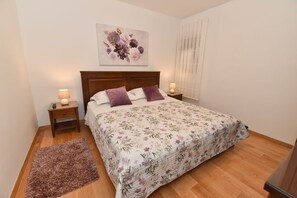 A bedroom with a wooden bed, floral bedding, two bedside lamps, a nightstand, a decorative rug, and a floral artwork on the wall.