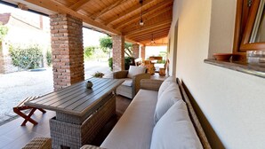 Une terrasse extérieure couverte, aménagée avec des meubles en osier, un pilier en briques et un plafond en bois.