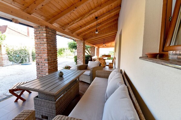 An outdoor covered patio with wicker furniture, a brick pillar, and a wooden ceiling.