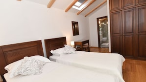 Une chambre avec deux lits, des têtes de lit en bois, une lucarne, une armoire et une salle de bain visible à travers une porte ouverte.