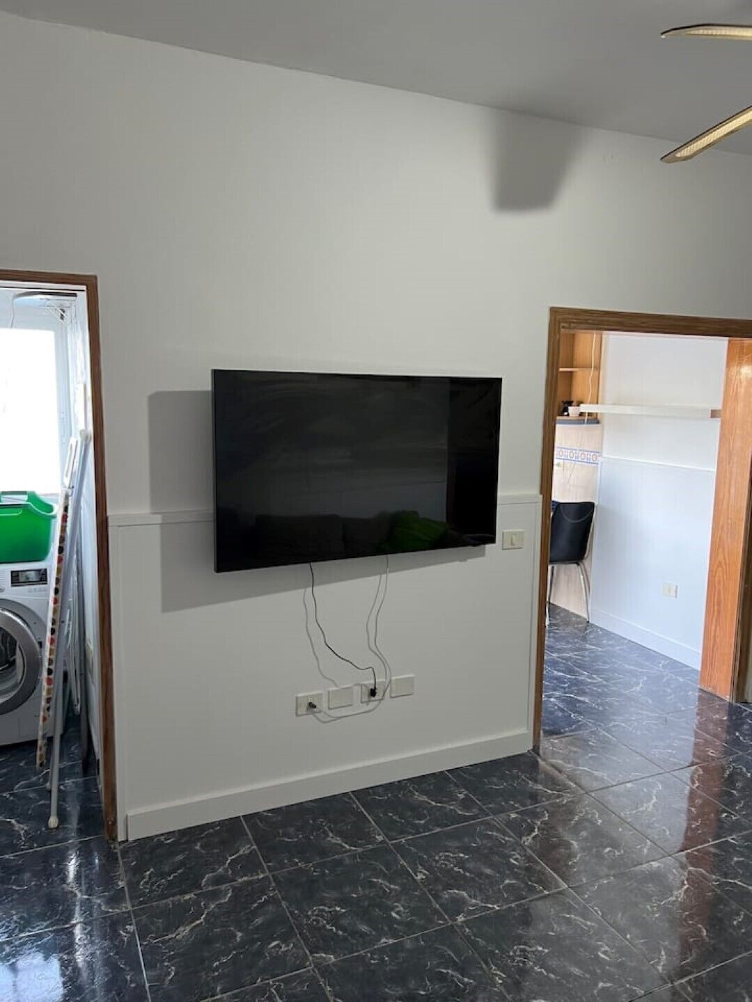 A room with a flat-screen TV mounted on the wall, a washing machine, and a tiled floor.