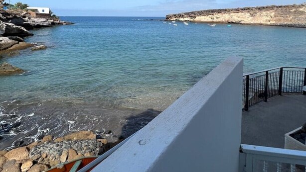 A coastal view with clear blue water, rocky shore, and a white building with a balcony. - Claudia Puertito de Adeje - 1 bedroom, 70sqm, on the beach (CN)