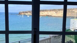 A view through a window with a grid pattern, overlooking a coastal area with boats and rocky terrain. - Claudia Puertito de Adeje - 1 bedroom, 70sqm, on the beach (CN)