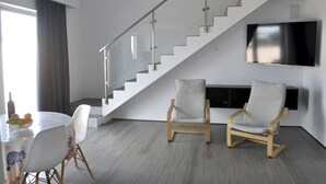 Un salon moderne avec un escalier, deux fauteuils, une table à manger avec des chaises et un téléviseur à écran plat fixé au mur.