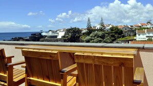 Une vue sur la mer avec des chaises en bois, un mur de pierre et des maisons en arrière-plan.