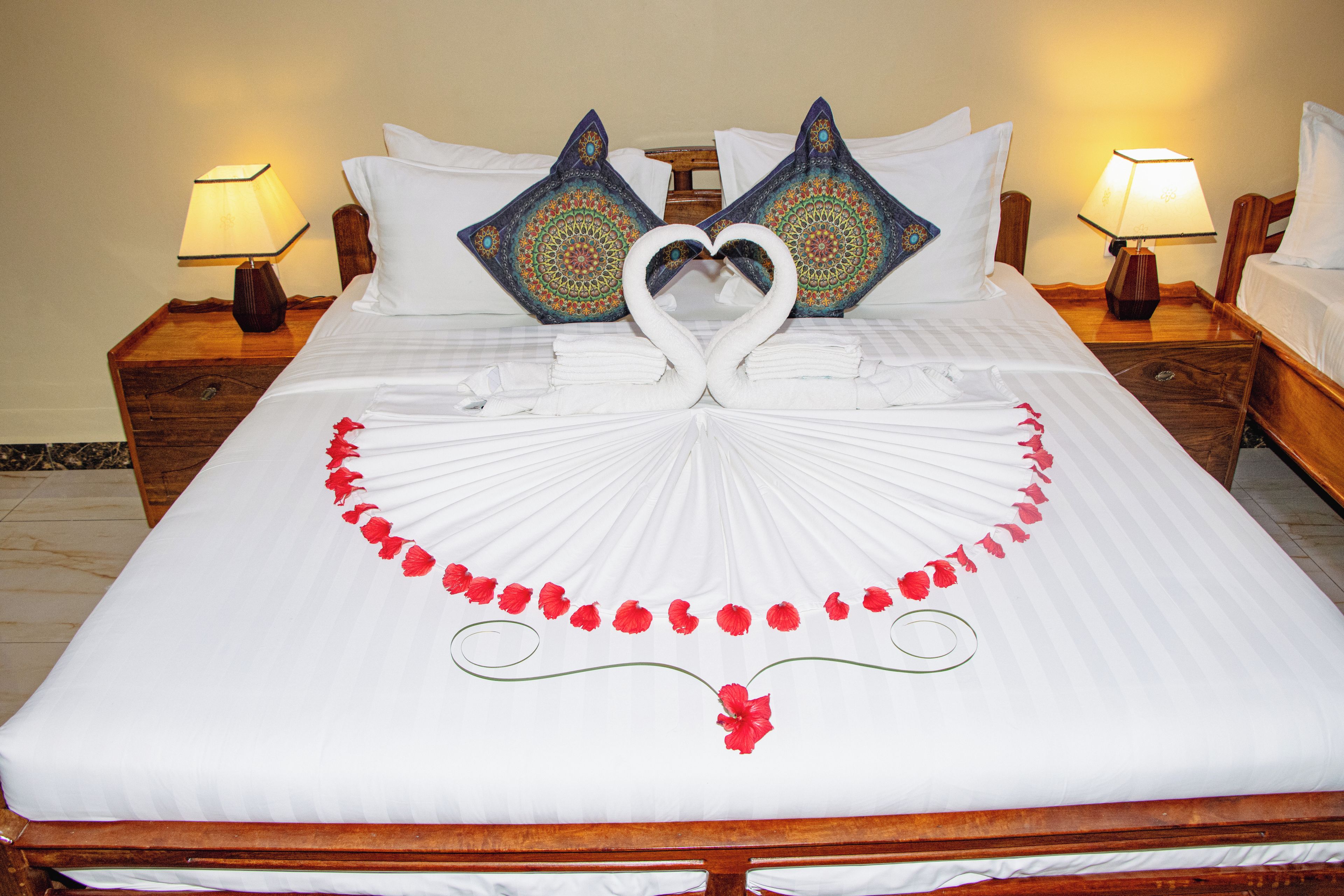 A neatly made bed with a heart-shaped towel arrangement and a decorative garland of red flowers.