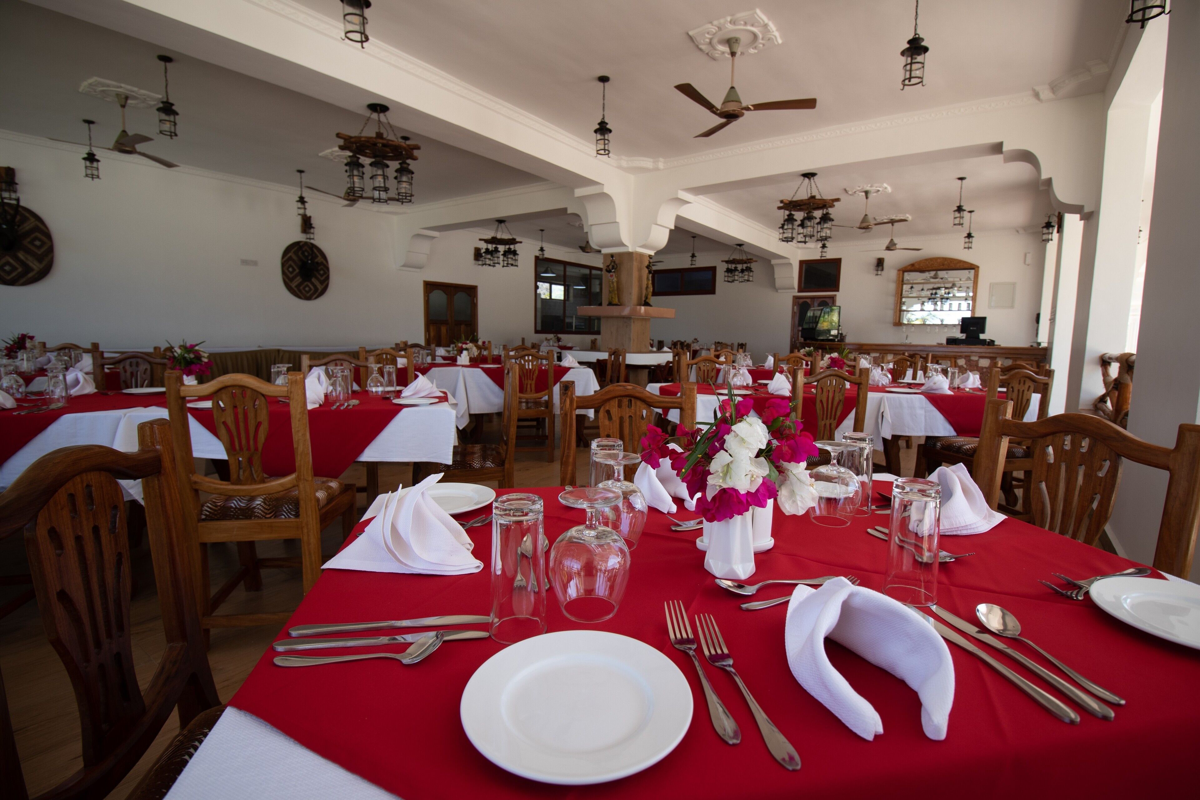 A restaurant with multiple tables set for dining, each with white tablecloths and red napkins.