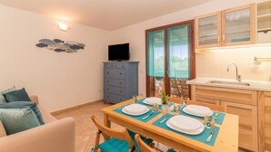 A dining area with a table set for two, a television, and a kitchen with wooden cabinets. - Glori House 50m From Marina di Olbia (Olbia)