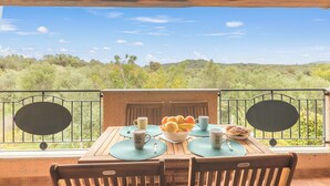 A wooden table with a bowl of fruit and pastries, two cups, and a spoon on a balcony with a view of green hills and a clear sky. - Glori House 50m From Marina di Olbia (Olbia)