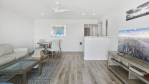 A modern living room with a sofa, a dining table, and a TV. - Luxury Beachfront Villa - Penthouse B (Carlsbad)