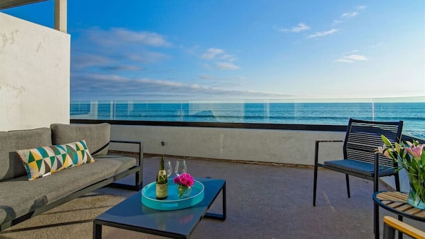 A balcony with a sofa, a coffee table, and a chair, overlooking a clear blue sea. - Luxury Beachfront Villa - Penthouse B (Carlsbad)