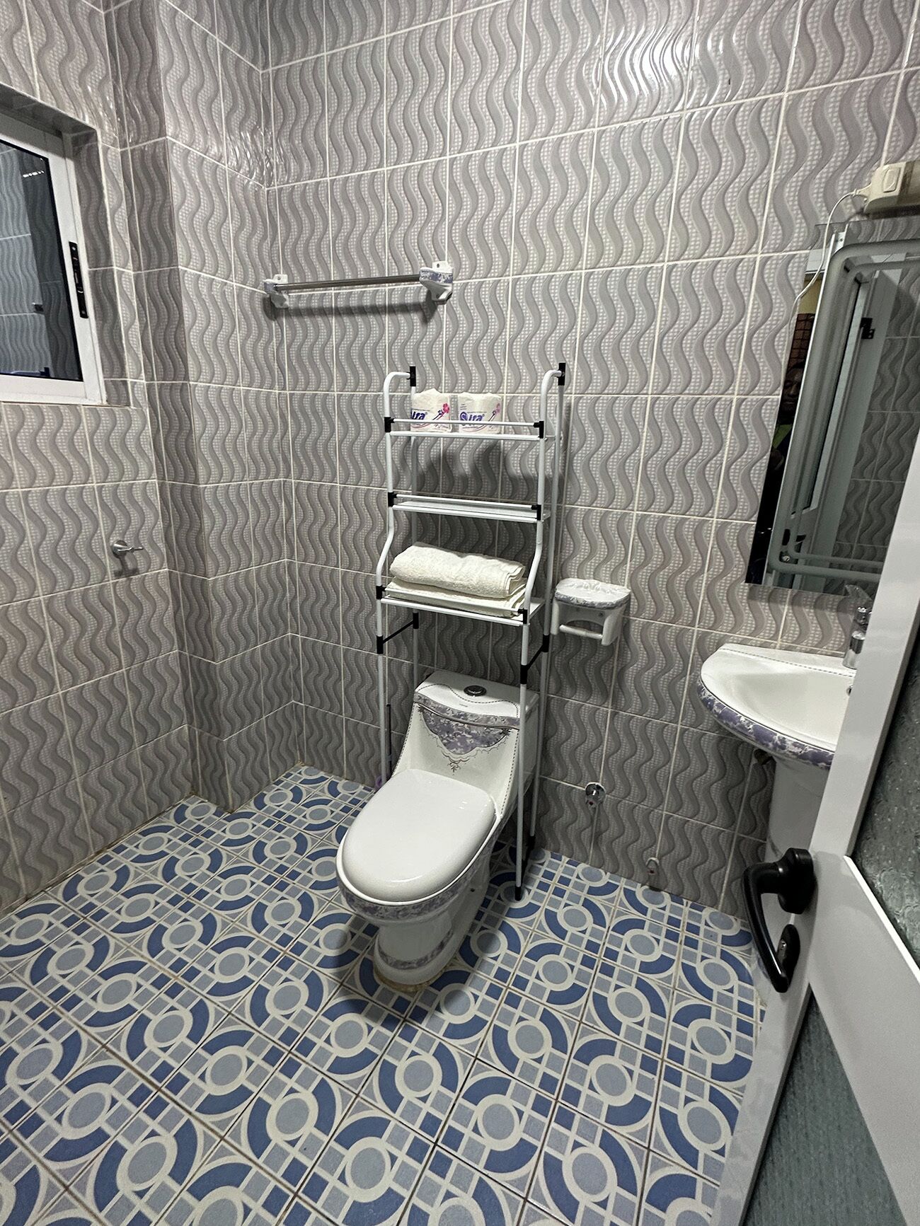 A bathroom with a toilet, a shelf with towels, and a sink with a mirror.
