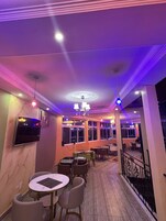 A restaurant interior with tables and chairs, a chandelier, and a TV mounted on the wall.