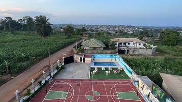 Una cancha de baloncesto al aire libre con césped verde, un edificio pequeño y vistas a un pueblo distante.