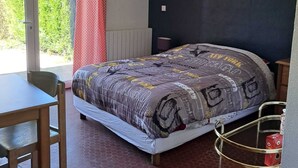 A bedroom with a bed, a table, and a chair. There is a window with a view of greenery outside. - Le Paradis de Marie (Treignac)