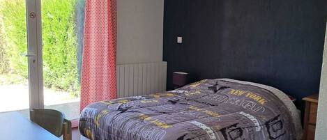 Une chambre à coucher avec un lit, une table et une chaise. Il y a une fenêtre qui donne sur un paysage verdoyant.