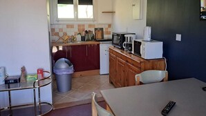 A compact kitchen with a microwave, toaster, and coffee maker on the counter, a trash bin, and a dining area with a table and chairs. - Le Paradis de Marie (Treignac)