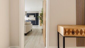 A modern living room with a sofa, a wooden side table, and a kitchen in the background. - Modern 2bed Flat, Parking, Close to Beach & Shops (Bournemouth)
