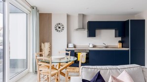 A modern kitchen with dark blue cabinets, a round glass table, and a dining area with wooden chairs. - Modern 2bed Flat, Parking, Close to Beach & Shops (Bournemouth)